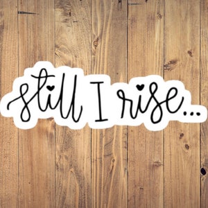 May include: A white sticker with black lettering that reads "still I rise..." with a small heart above the word "still" and another small heart above the word "rise".