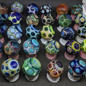 May include: A collection of 20 colorful glass marbles with intricate patterns. Each marble has a unique design featuring various colors and shapes, including blue, green, red, and white.