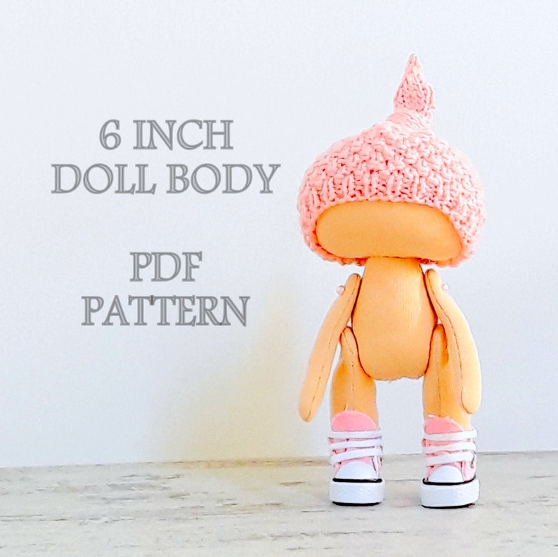 Op de afbeelding: Een PDF-patroon voor een 15 cm poppenlichaam. De pop draagt ​​een roze gebreide muts en roze sneakers.