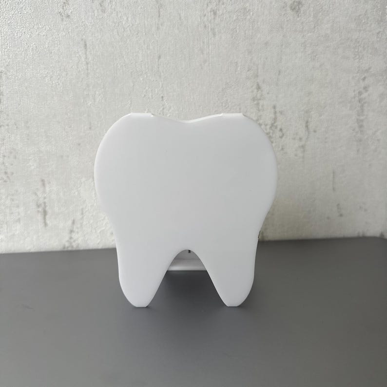 May include: A white plastic tooth-shaped container.