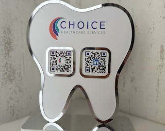 May include: A white tooth-shaped sign with a silver border. The sign has the text "CHOICE" in blue and "HEALTHCARE SERVICES" in black. There are two QR codes on the sign, one with the word "CHOICE" and the other with the LinkedIn logo.
