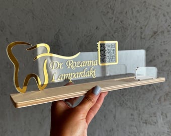May include: A clear acrylic desk sign with a gold tooth graphic and the text "Dr. Rozanna Lampardaki". A small square QR code is also on the sign.