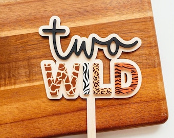 May include: Two Wild cake topper with a black script font for the word "two" and the word "WILD" in brown, orange, and black animal print letters.