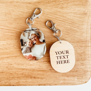 May include: Two oval wooden keychains. One keychain features a photo of a woman and a child. The other keychain has the text "YOUR TEXT HERE" engraved on it.