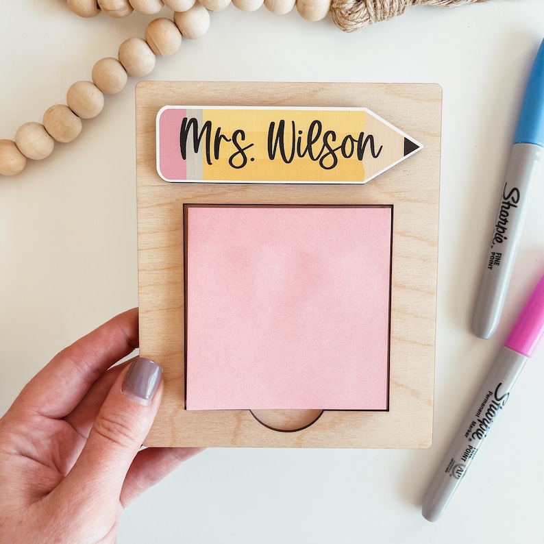 May include: A wooden desk organizer with a pink sticky note pad and a yellow pencil with the text "Mrs. Wilson" on it.