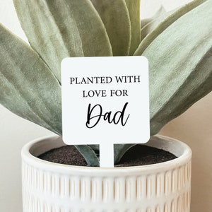 May include: White square plant marker with black text that reads "Planted with love for Dad".
