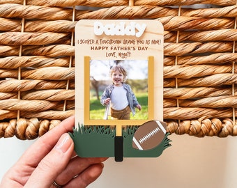 May include: A wooden sign with a football goalpost design and a photo frame. The sign says "Daddy I scored a touchdown having you as mine! Happy Father's Day Love, Wyatt".