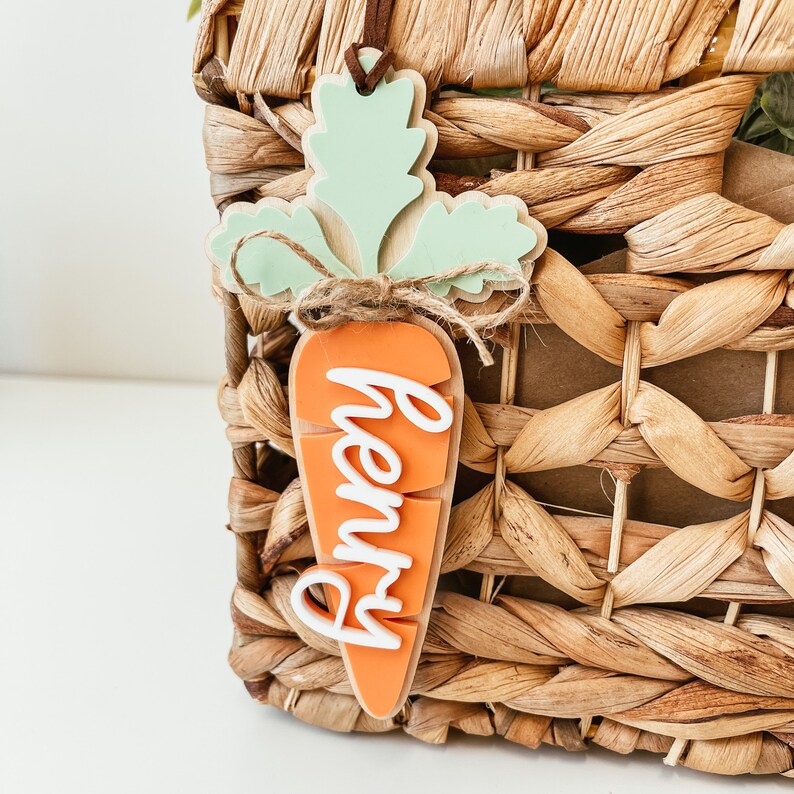 May include: A wooden carrot-shaped ornament with a green leafy top and the name "Henry" written in white on the orange carrot.