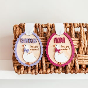 May include: Two purple and red wooden Easter egg ornaments with white duck designs. The ornaments have the names "Chandler" and "Flora" and the text "happy easter!" on them.