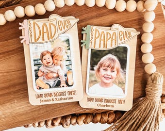May include: Two wooden photo frames with the words "Best Dad Ever" and "Best Papa Ever" on top. Each frame holds a photo of a child. The bottom of each frame reads "Love Your Biggest Fans!" and the names of the children.