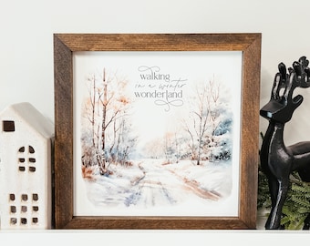 May include: A framed watercolor painting of a snowy forest path with the text "walking in a winter wonderland". The frame is brown wood with a white mat.