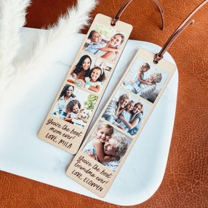 May include: Two wooden photo bookmarks with a vertical layout of four photos each. The bookmarks have a brown leather strap. The top bookmark has photos of a mother and daughter, and the bottom bookmark has photos of a grandmother and granddaughter. The text on the bookmarks reads "You're the best Mom ever! LOVE, MILA" and "You're the best Grandma ever! LOVE, ELOWYN".