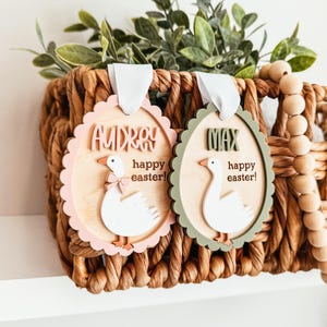 May include: Two wooden Easter ornaments shaped like eggs with a goose design. The pink ornament says "Audrey happy easter!" and the green ornament says "Max happy easter!"