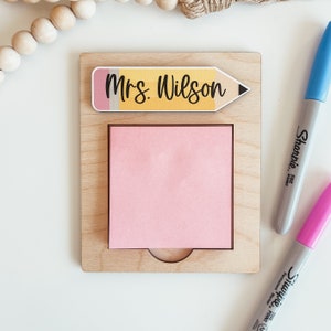 May include: A wooden desk organizer with a pink sticky note and a yellow pencil with the text "Mrs. Wilson" on it.