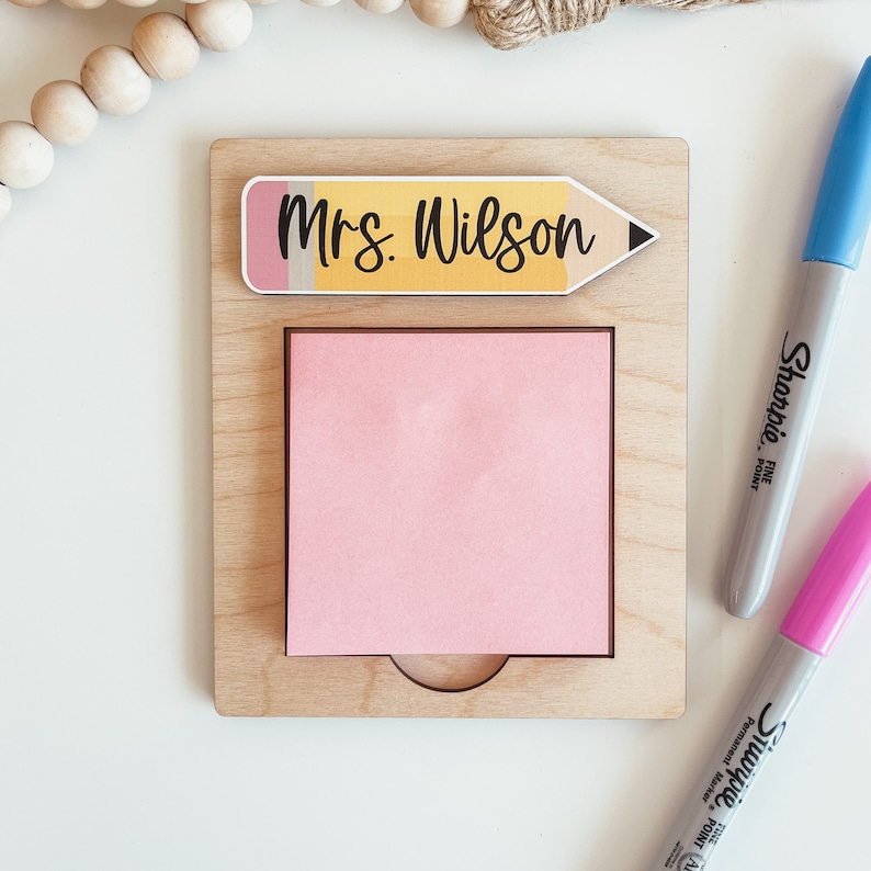 May include: A wooden desk organizer with a pink sticky note and a yellow pencil with the text "Mrs. Wilson" on it.