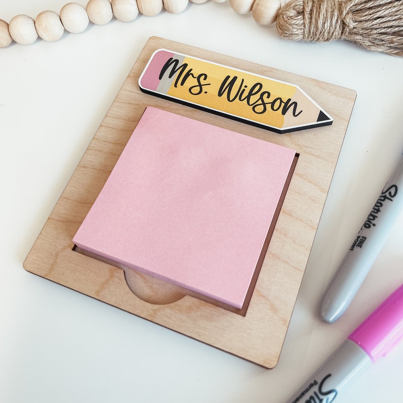 May include: A wooden desk organizer with a pink sticky note and a yellow pencil with the text "Mrs. Wilson" on it.