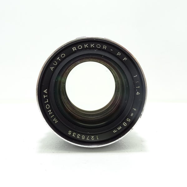 以下が含まれることがあります： ミノルタ Auto Rokkor-PF 58mm f/1.4 カメラレンズ。レンズは黒とシルバーのアクセントで、「Minolta Auto Rokkor-PF 1:1.4 f=58 mm」の文字とシリアル番号1276335が記されています。