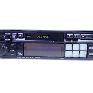 May include: Black Alpine car stereo with buttons, knobs, and a digital display. Features include treble, bass, and program controls. The text "ALPINE" is visible on the face of the stereo. Model number 7190ET is also visible.