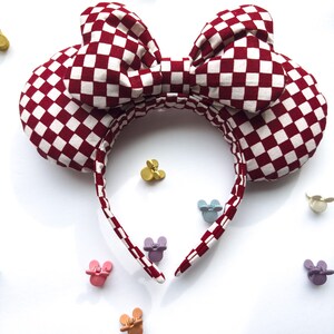 May include: Red and white checkered fabric headband with a large bow. The headband is shaped like Mickey Mouse ears.