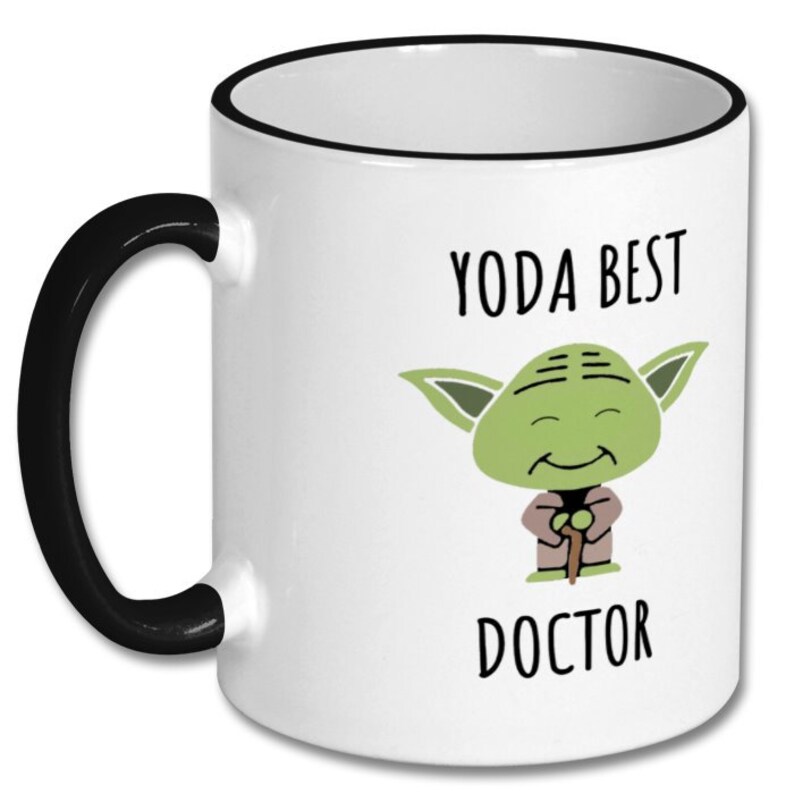 May include: White ceramic coffee mug with a black handle and rim. The mug features a cartoon image of Yoda from Star Wars with the text "Yoda Best Doctor".