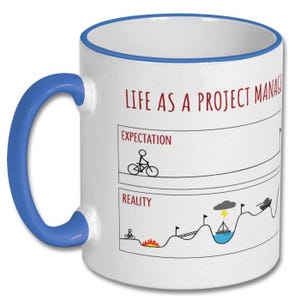 May include: White ceramic mug with a blue handle and rim. The mug features the text "LIFE AS A PROJECT MANAGER" in red, along with a humorous comparison of expectations versus reality, illustrated with stick figures and a bicycle.