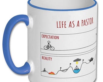 May include: White ceramic mug with a blue handle and rim. The mug features the text "LIFE AS A PASTOR" in red, along with a humorous illustration comparing expectations to reality, including a cyclist and a boat.