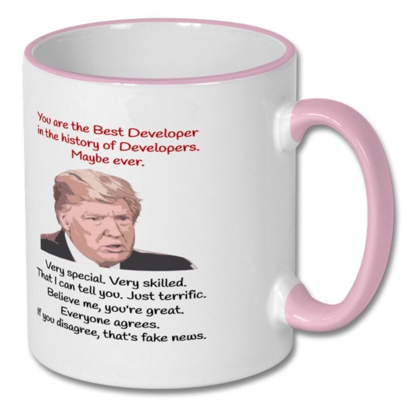 May include: White coffee mug with a pink rim and handle. The mug features a cartoon image of Donald Trump and the text "You are the Best Developer in the history of Developers. Maybe ever. Very special. Very skilled. That I can tell you. Just terrific. Believe me, you're great. Everyone agrees. If you disagree, that's fake news."