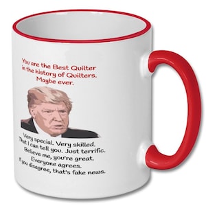May include: White ceramic coffee mug with a red rim and handle. The mug features a humorous quote about quilting with a picture of a man with blonde hair. The text reads: "You are the Best Quilter in the history of Quilters. Maybe ever. Very special. Very skilled. That I can tell you. Just terrific. Believe me, you're great. Everyone agrees. If you disagree, that's fake news."