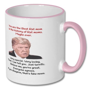 May include: White ceramic coffee mug with a pink rim and handle. The mug features a red and white graphic of a man with the text "You are the Best Rat mom in the history of Rat moms. Maybe ever. Very special. Very loving. That I can tell you. Just terrific. Believe me, you're great. Everyone agrees. If you disagree, that's fake news."