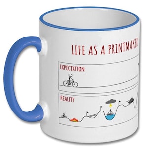 May include: White ceramic mug with a blue handle and rim. The mug features the text "LIFE AS A PRINTMAKER" in red, along with a humorous graphic comparing expectations to reality, including a cyclist and a boat.