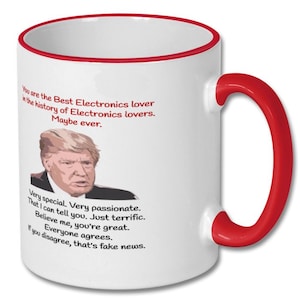 May include: White ceramic coffee mug with a red rim and handle. The mug features a humorous quote about electronics lovers, with a picture of a man with blonde hair. The quote reads: "You are the Best Electronics lover in the history of Electronics lovers. Maybe ever. Very special. Very passionate. That I can tell you. Just terrific. Believe me, you're great. Everyone agrees. If you disagree, that's fake news."