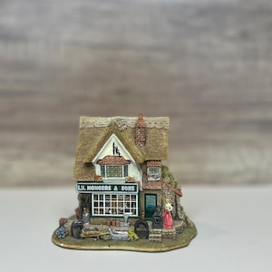 May include: A miniature cottage with a thatched roof and a sign that reads "L.M. Mongers & Sons". The cottage has a small window and a door with a woman standing in front of it. The cottage is made of ceramic and is painted in a variety of colors.
