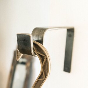 May include: A metal hook with a black finish, mounted to a wall. A beige plastic hanger is hanging from the hook.