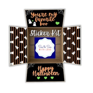 May include: A cardboard box with a black and orange striped pattern and ghost illustrations. The box is open and the inside says "You're my favorite boo" and "Sticker Kit". The bottom of the box says "Happy Halloween" with green hearts.