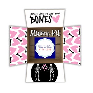 May include: Open box with a sticker kit inside. The box is decorated with a pink and white pattern of hearts and bones. The sticker kit includes a sticker with two skeletons holding hands and hearts, and a sticker with the text "Sea to Sea with Love". The text on the box reads "I can't wait to jump your bones".