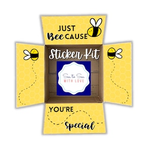 May include: A yellow cardboard box with a bee design and the text "Just Bee Cause Sticker Kit" and "You're Special". The box is open and a blue sticker with the text "Sea to Sea With Love" is visible inside.