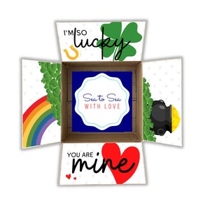 May include: A white box with a blue and white label that says "Sea to Sea with Love". The box is open and the inside is decorated with a rainbow, shamrocks, a pot of gold, and a horseshoe. The box also has the text "I'm so lucky" and "You are mine".