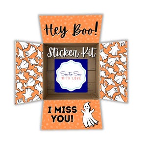 May include: An orange and white cardboard box with a ghost pattern. The box is open and says "Hey Boo! Sticker Kit" on the top flap. The inside of the box says "I Miss You!" and has a ghost sticker on the bottom flap. The box also has a blue and white sticker that says "Sea to Sea with Love."