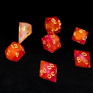 Könnte beinhalten: Sieben mehrseitige Würfel in Rot- und Orangetönen mit goldenen Zahlen. Die Würfel liegen auf einem schwarzen Hintergrund, wobei verschiedene Zahlen sichtbar sind. Geeignet für Rollenspiele.