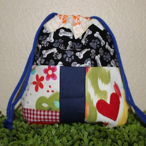 Könnte beinhalten: Ein Patchwork-Beutel mit Kordelzug und blauem Kordel. Die Tasche hat verschiedene Stoffmuster, darunter Hundeknochen auf Schwarz, rote Blumen und ein rotes Herz. Die Tasche ist zum Tragen von Gegenständen konzipiert.