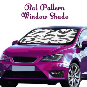 May include: A black and white bat pattern car sunshade. The sunshade is in a car windshield. The car is pink.