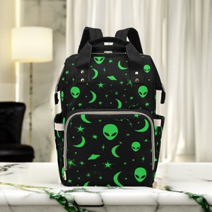 May include: Black backpack with a green alien, crescent moon, and star pattern.
