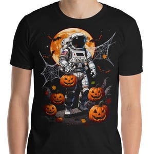 May include: A black t-shirt featuring a graphic of an astronaut in a white space suit walking on a lunar surface. The astronaut is surrounded by orange jack-o'-lanterns, spider webs, and bats, set against a large, glowing orange full moon.