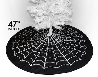 May include: A circular black tree skirt featuring a white spider web pattern. The fabric accessory measures 47 inches in diameter and is positioned around the base of a white artificial tree, providing a decorative cover for the stand.