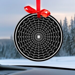 May include: A black and white spiderweb design car ornament with a red ribbon.