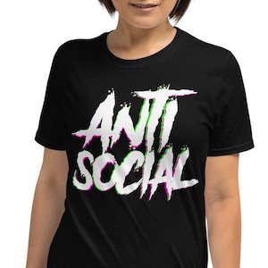Puede incluir: Camiseta negra de manga corta con un gr&aacute;fico blanco que dice "ANTI SOCIAL" en una fuente estilizada con acentos verdes y morados.