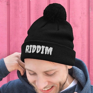 May include: A black beanie with a white pom pom on top and the word "RIDDIM" embroidered on the front in white.