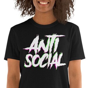 Puede incluir: Camiseta negra de manga corta con un gr&aacute;fico blanco que dice "ANTI SOCIAL" en una fuente con efecto glitch con acentos verdes y morados.