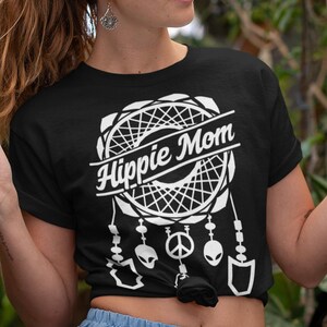 Może przedstawiać: Kobieta w czarnym t-shircie z białym wzorem łapacza sn&oacute;w i napisem "Hippie Mom". Ma na sobie niebieską sp&oacute;dnicę i trzyma biały kubek.