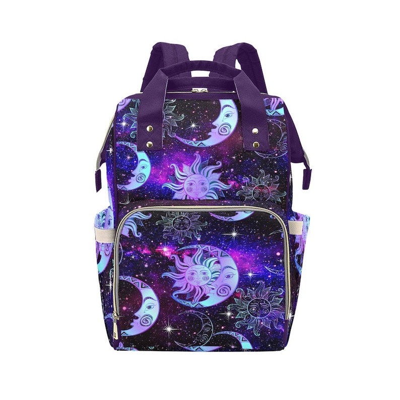 May include: Purple diaper bag with a galaxy print featuring moons and suns. The bag has a zippered top closure and multiple pockets.
